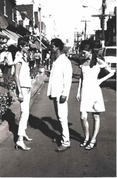 Three stylish individuals converse on a city street, dressed in monochrome, fashionable attire.